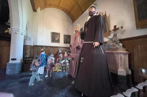 Inside a church with giant statues of friars towering over visitors as they tour a display area.