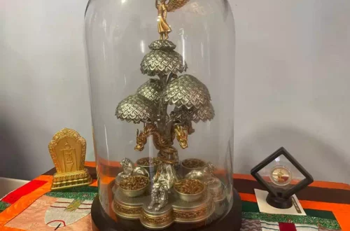Metallic tree sculpture under a glass dome, with a winged figure on top and small coin bowls at the base.