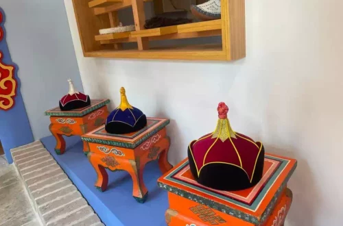 Three ornate orange pedestals with colorful crown-shaped hats on display along a blue platform, shelf with shoes in the background.