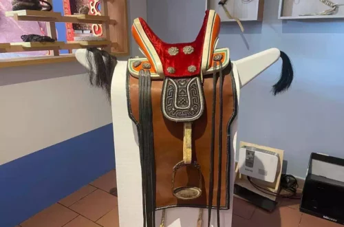 Decorative Western saddle displayed on a stand with red felt and ornate silver embroidery, in a shop or gallery setting.